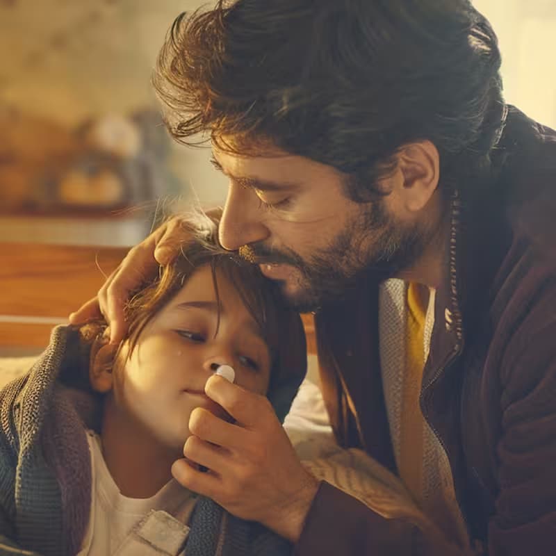 Escena de un padre cuidando a su hijo con cariño durante una enfermedad leve en el hogar.